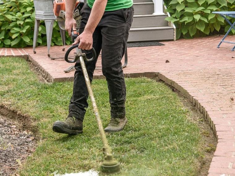 Crew member edging a garden bed along a brick walkway